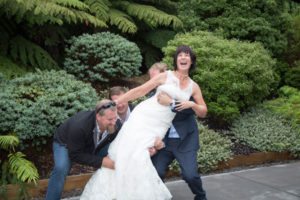 laughing bride being picked up by groom and her brothers in bush setting